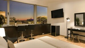 Une chambre d’hôtel moderne dotée d’une grande fenêtre donnant sur la ville, d’un bureau avec une chaise, d’un lit et d’un téléviseur à écran plat fixé au mur.