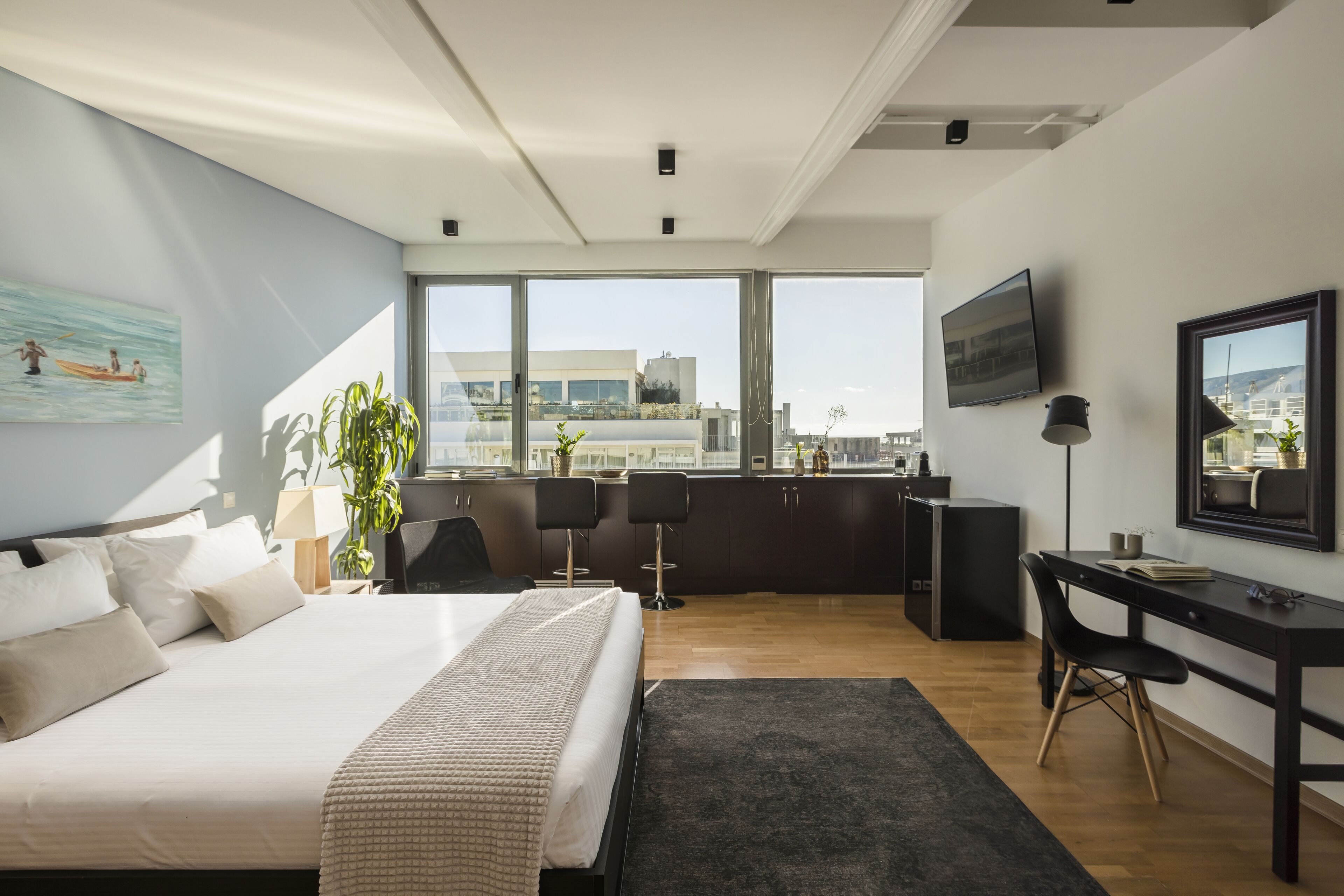 A modern hotel room with a large bed, a desk, and a view of the city.
