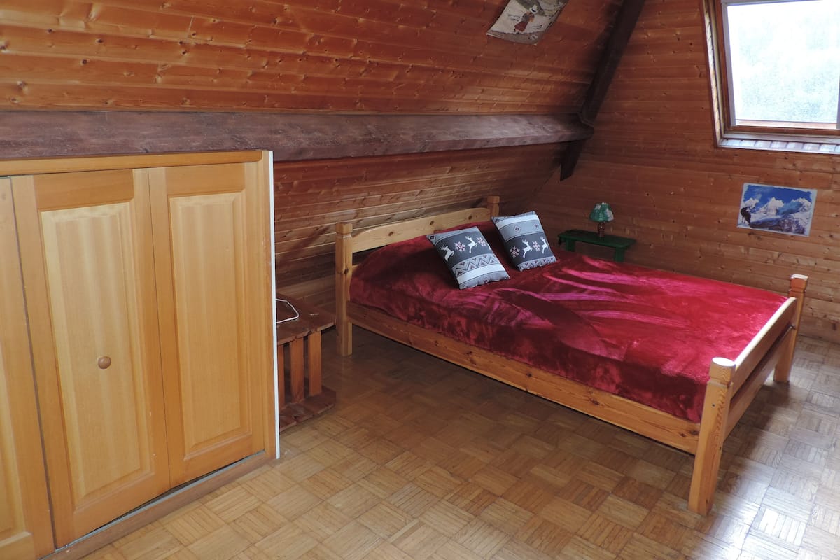 A wooden cabin room with a bed, a wooden wardrobe, and a window.