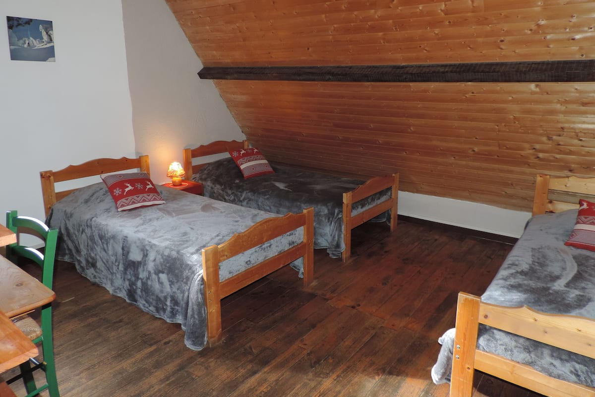 A cozy room with two wooden beds, a green chair, and a small table.