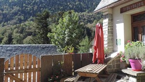 A wooden deck with a table and chairs, a red umbrella, and a mountain backdrop. - Le Barbajou (Aragnouet)