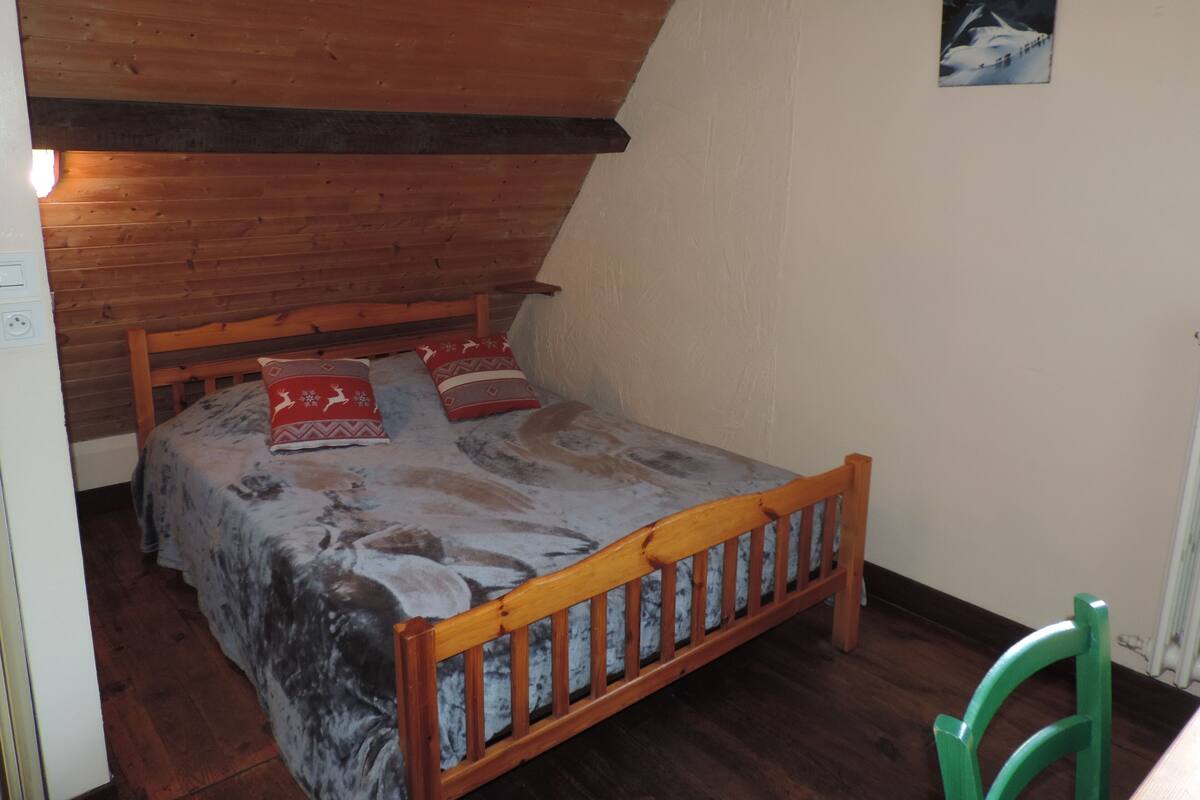 A bedroom with a wooden bed, a green chair, and a painting on the wall.