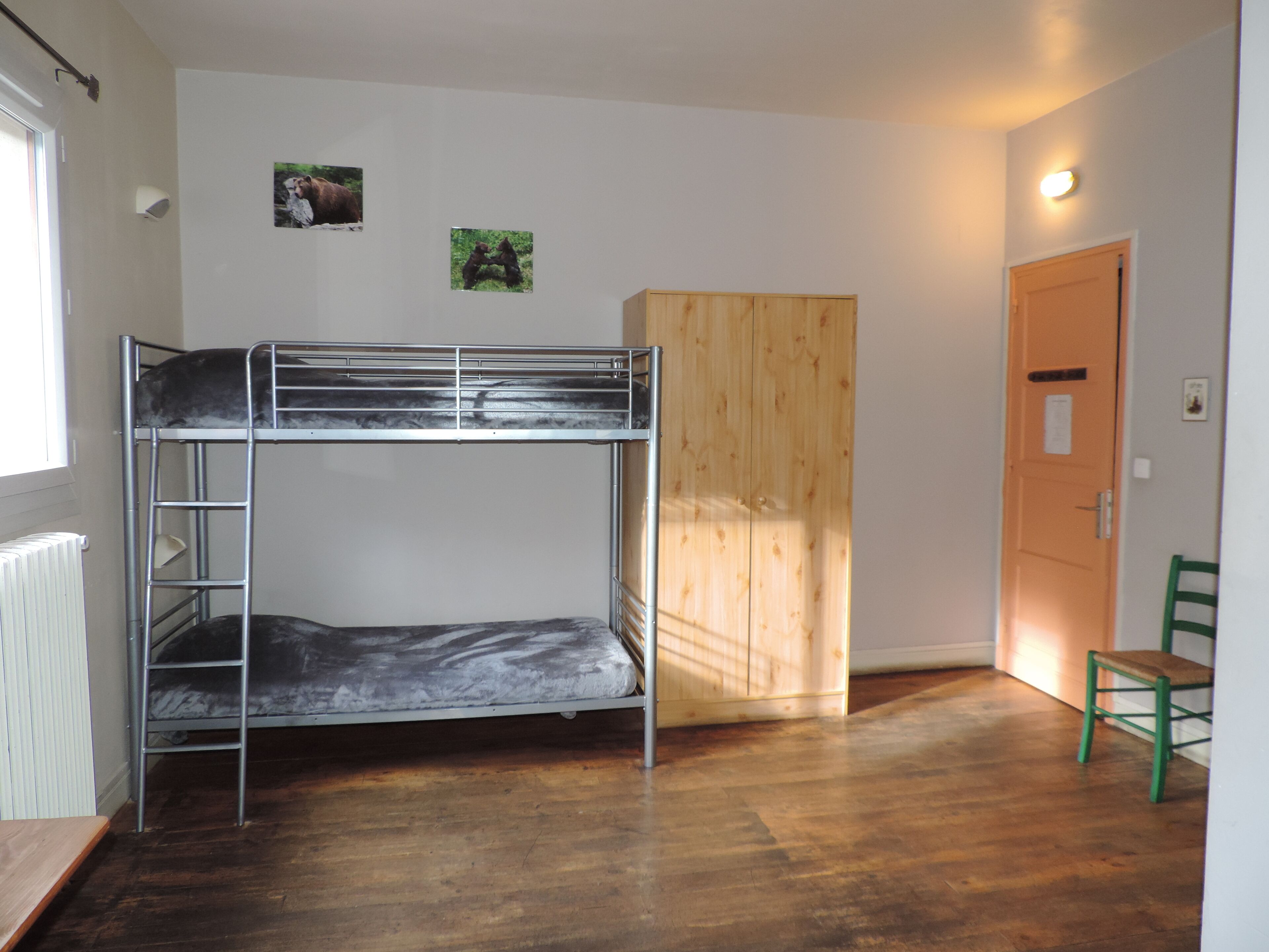 Habitación con literas, un armario de madera, una silla verde y dos cuadros en la pared.