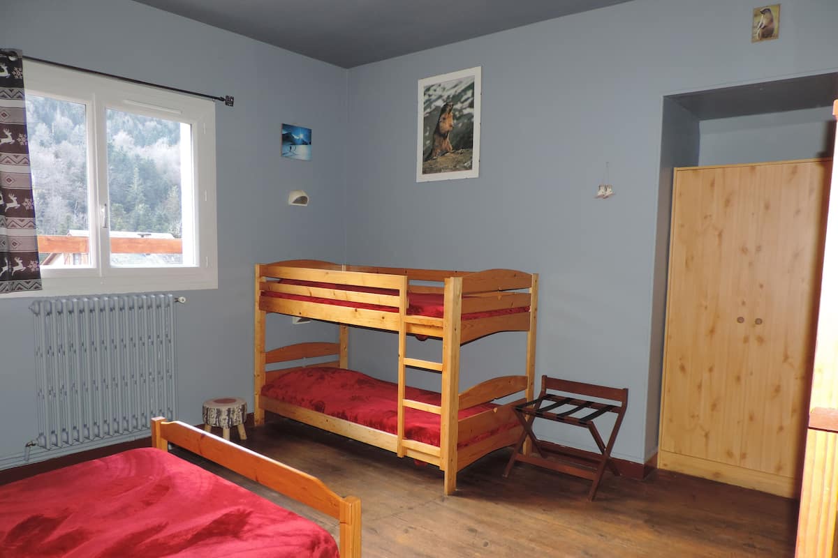 A bunk bed room with a wooden wardrobe and a window with a view of trees.