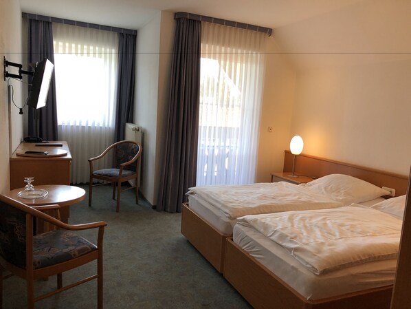 Habitación de hotel con cama, escritorio con lámpara, silla y ventana con cortinas.