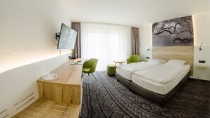 A hotel room with a bed, a desk, a chair, a small table, a TV, and a painting on the wall. - Landgasthaus Fischer (Suthfeld)