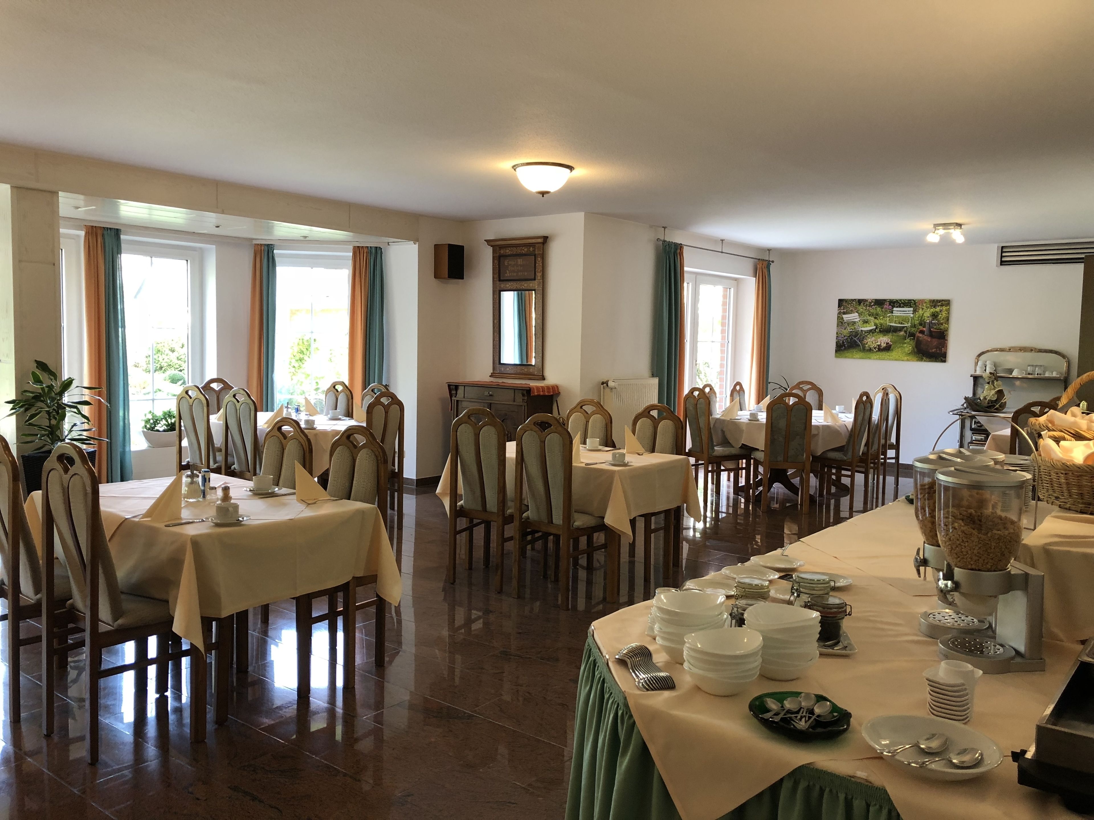 A dining area with multiple tables and chairs, a buffet setup, and a view of the outdoors through large windows.