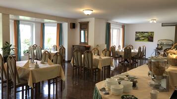 A dining area with multiple tables and chairs, a buffet setup, and a view of the outdoors through large windows.
