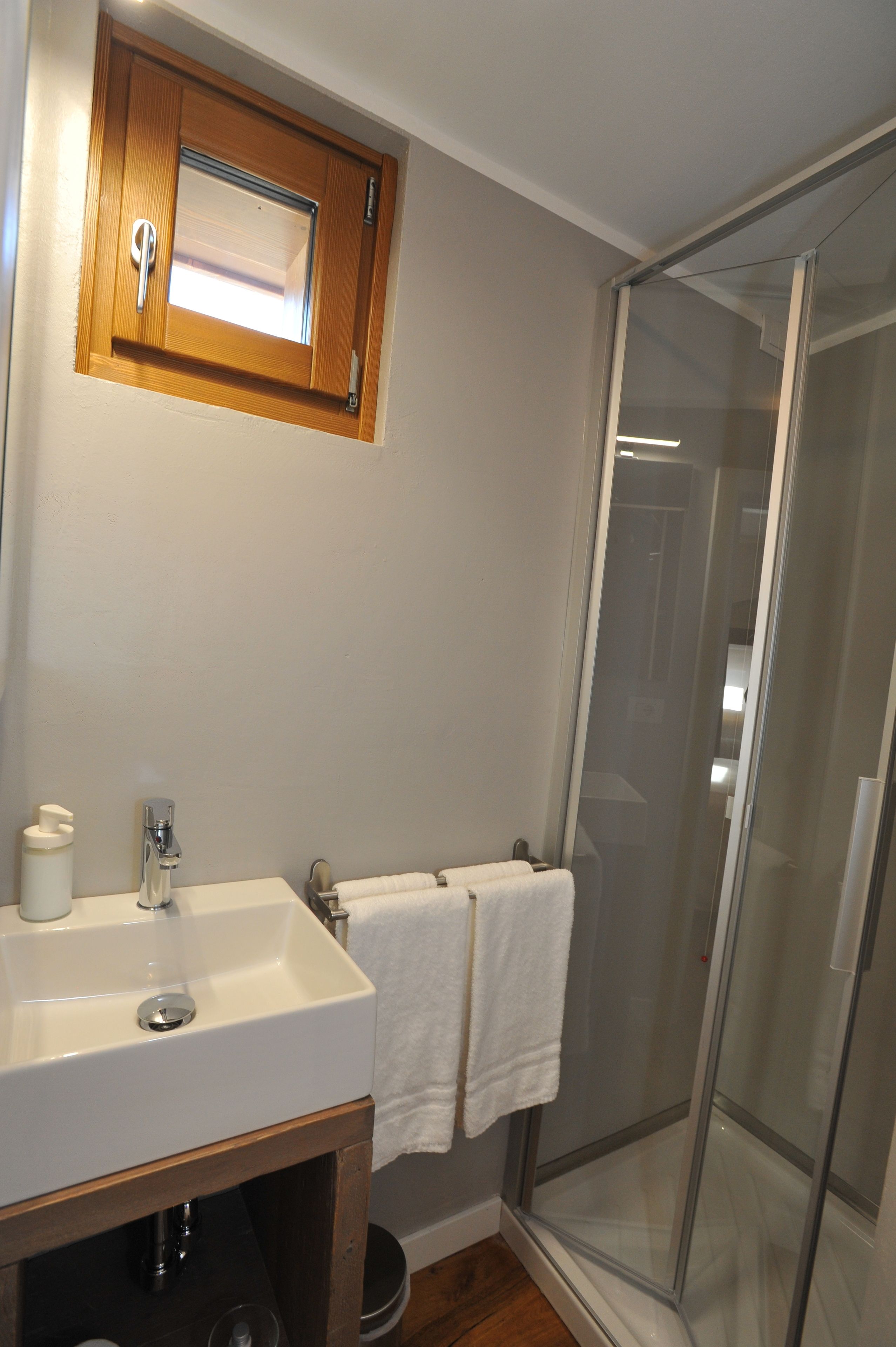A bathroom with a white sink, wooden cabinet, and a glass shower enclosure.