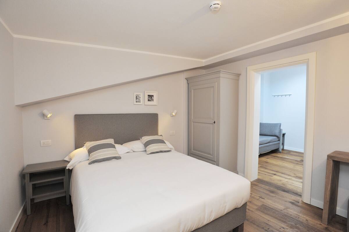 A bedroom with a bed, bedside tables, a wardrobe, and a view to a living area.
