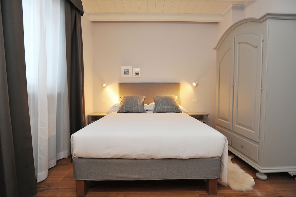 A neatly made bed with a grey headboard and pillows, a white bedside table with a lamp, and a white wardrobe with a mirror.