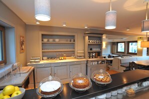 A modern kitchen with a buffet setup, including a counter with covered desserts and a bowl of fruit. - Baita Fanti Ski & Bike (Bormio)