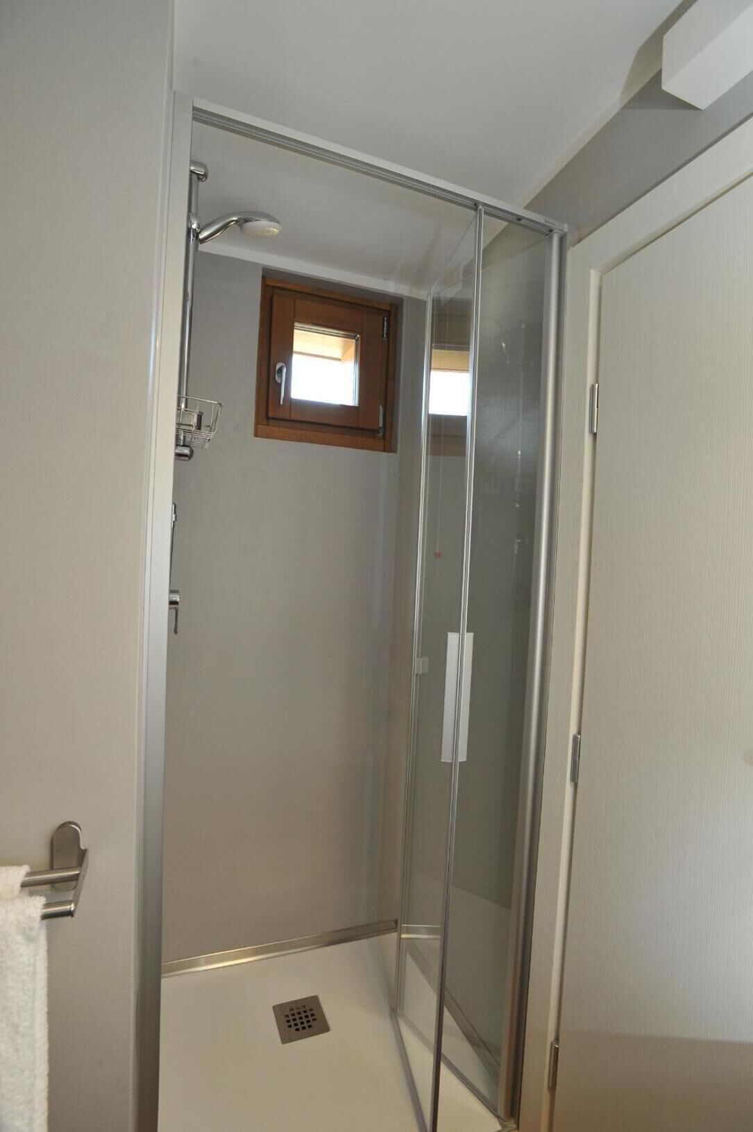 Una ducha a nivel con puerta de cristal, una ventana pequeña y un perchero para toallas.