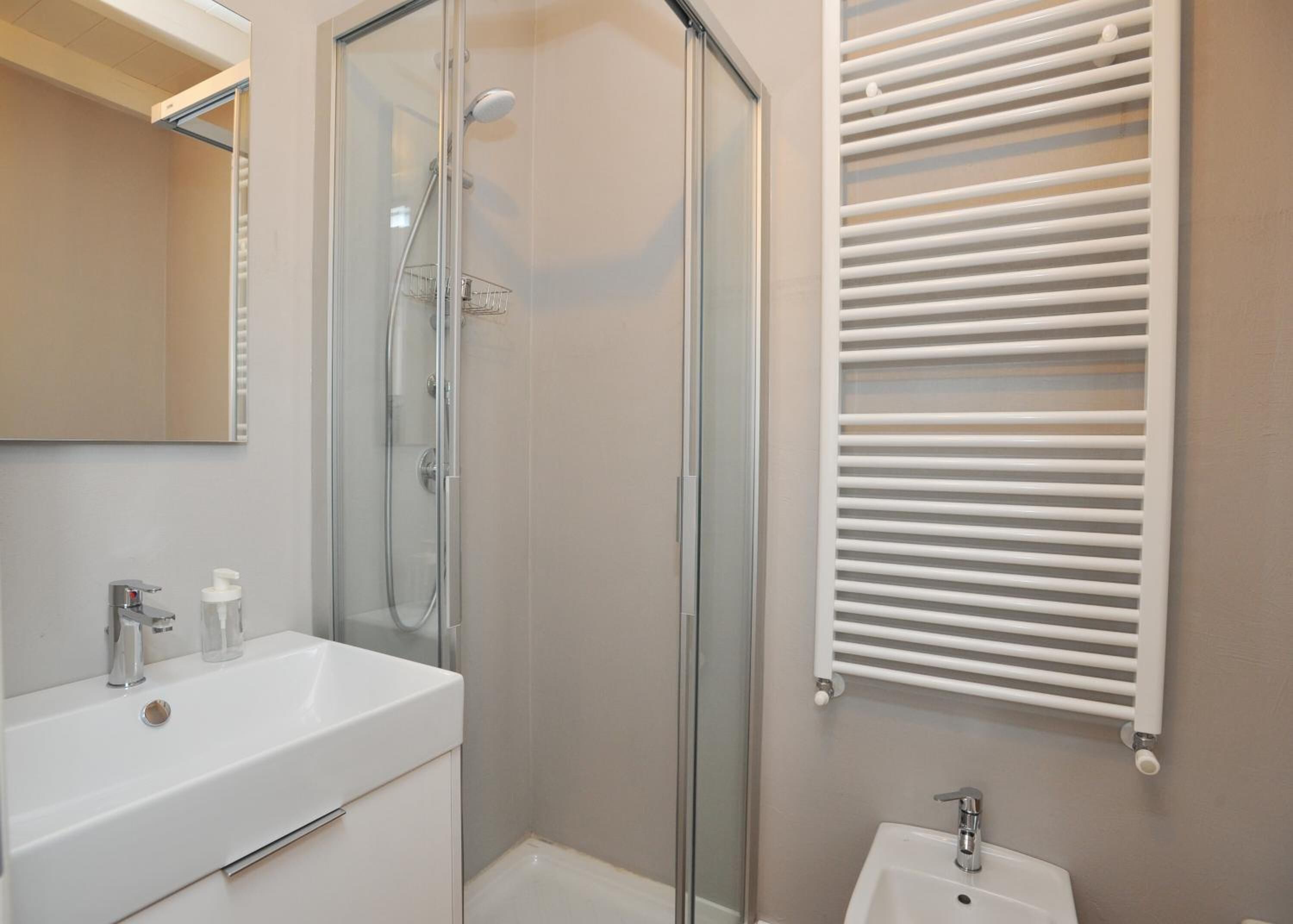 Une salle de bain moderne avec une douche à parois de verre, un lavabo blanc et un porte-serviettes avec des barres horizontales.