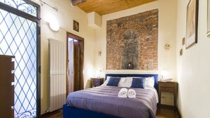A bedroom with a large bed, wooden flooring, a brick wall, and a decorative light fixture. - Florence Ariento Romantic Apartment (Florence)