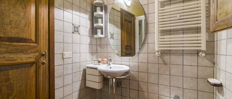 A bathroom with a wooden door, a white sink with a mirror above it, a bidet, and a tiled wall.