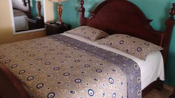 A bedroom with a wooden bed, patterned bedspread, a mirror, and a nightstand with a lamp.