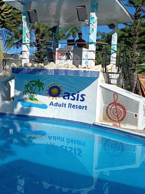 A swimming pool with a mural of palm trees and a sun, labeled "Oasis Adult Resort."