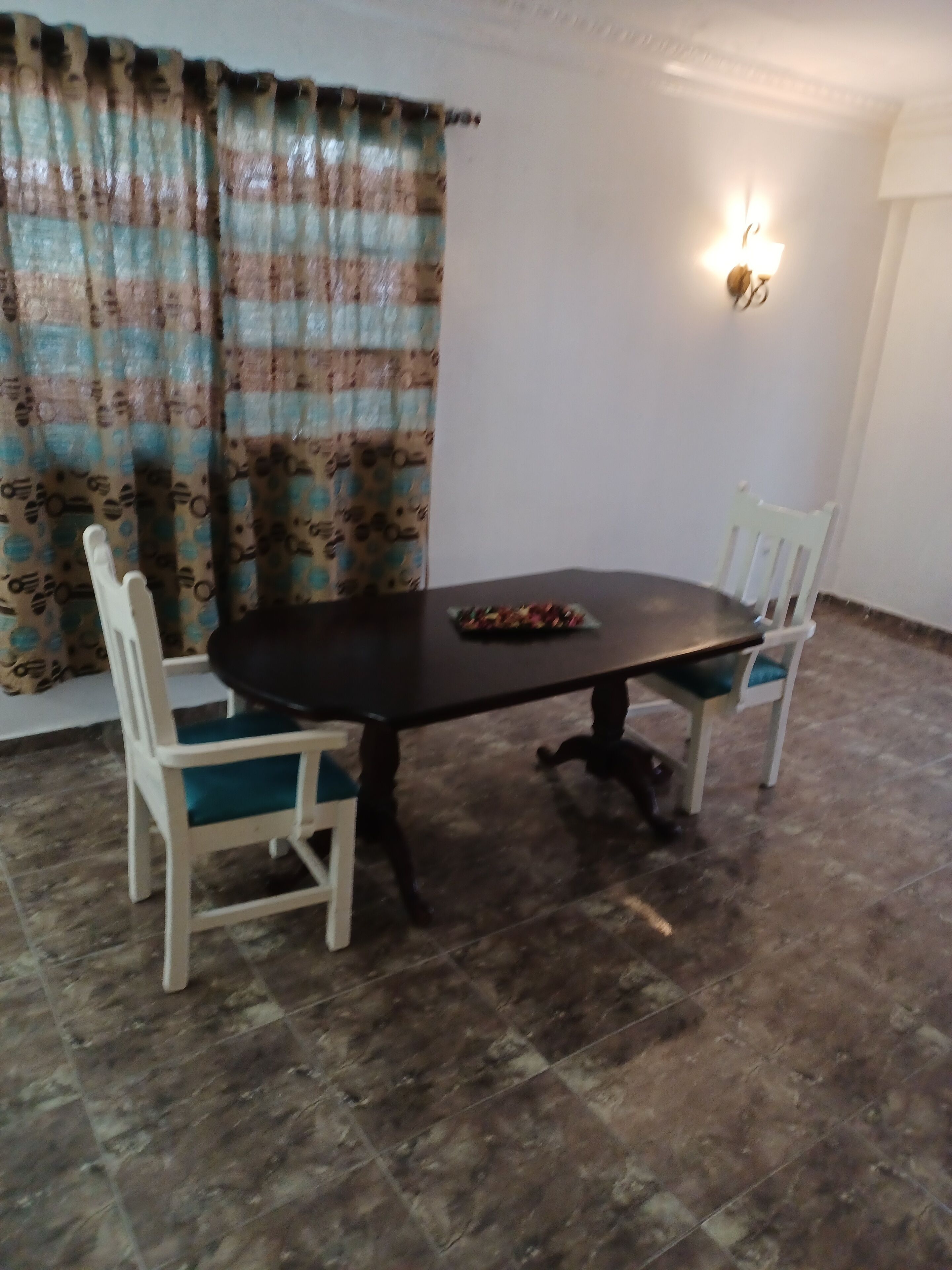 A dining area with a dark wooden table and two white chairs with teal cushions.