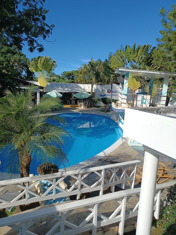 A swimming pool surrounded by palm trees and a shaded area with umbrellas.
