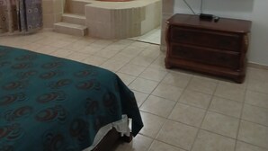 A bedroom with a bed, a television, a wooden dresser, and a bathtub. - Oasis Adult Resort (Puerto Plata)