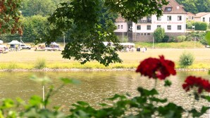 A building with a sign reading "Rudzevein Bodenwerder" in front of a body of water, surrounded by greenery. - Hotel Weserstuben (Bodenwerder)