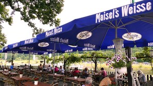 Outdoor seating with tables and chairs under blue umbrellas with the text "Maisel's Weisse". - Hotel Weserstuben (Bodenwerder)