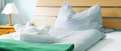 A neatly made bed with white and green linens, a wooden headboard, and a bedside lamp.