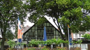 A traditional half-timbered building with a garden in front, surrounded by trees. - Hotel Weserstuben (Bodenwerder)
