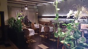 A restaurant with round tables and chairs, potted plants, and hanging lights. - Hotel Weserstuben (Bodenwerder)