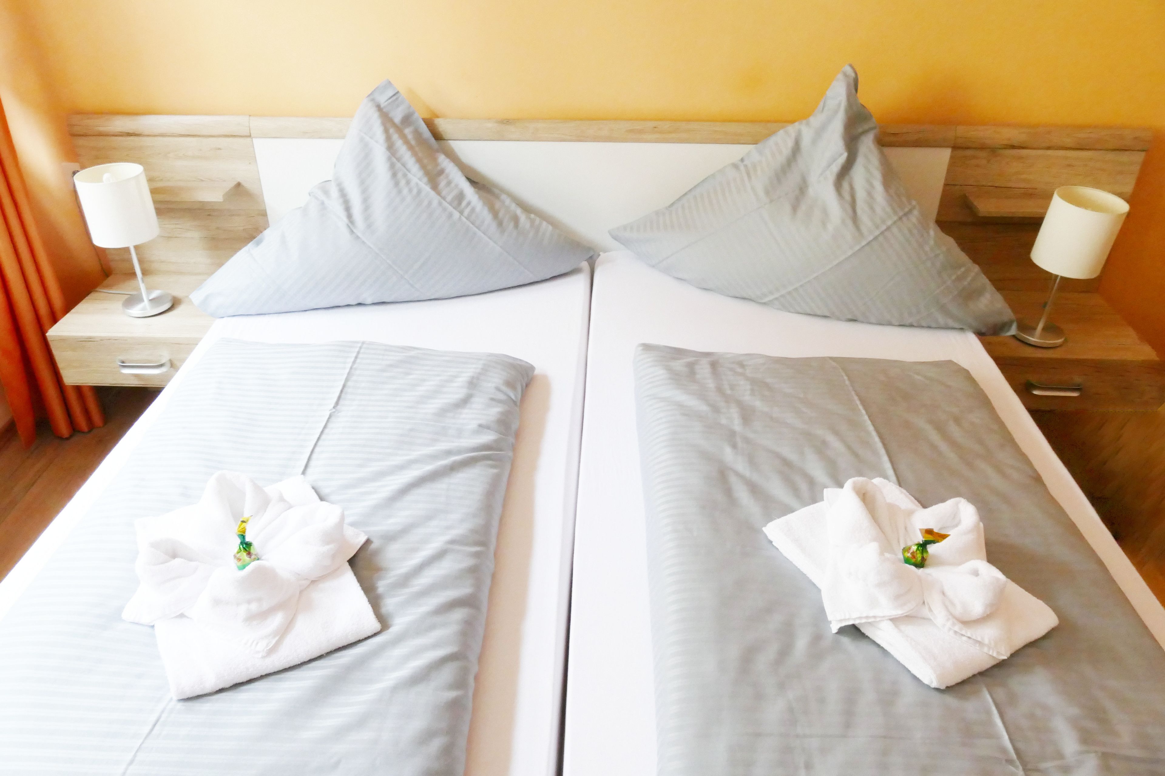 Un lit double avec du linge de lit et des oreillers gris, deux tables de chevet avec des lampes et une tête de lit en bois.