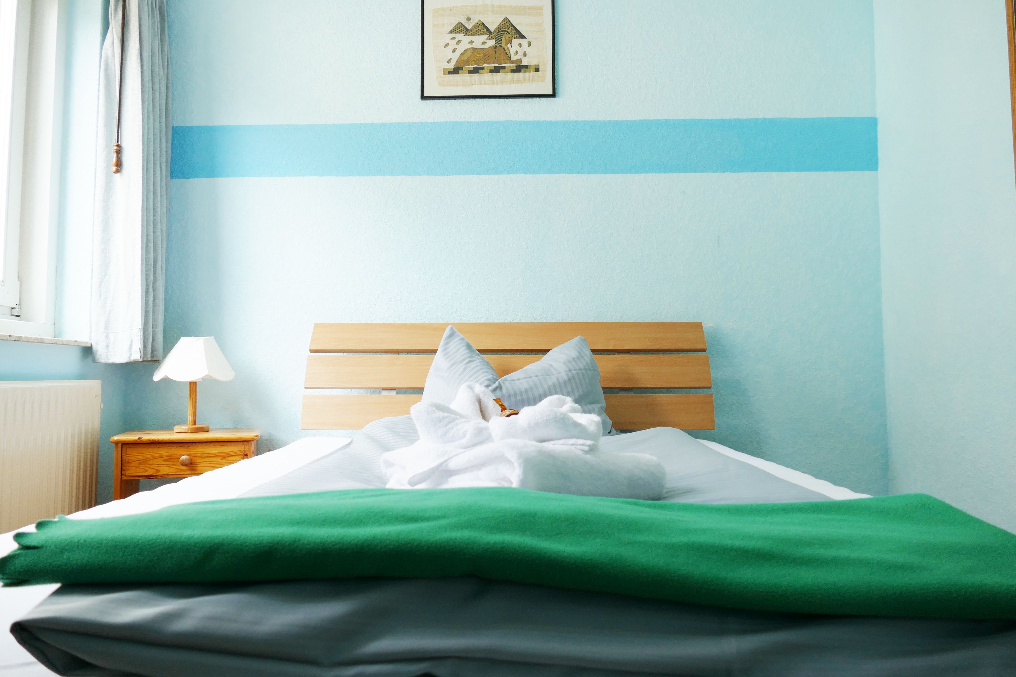 A neatly made bed with white and green linens, a wooden headboard, and a small bedside table with a lamp.