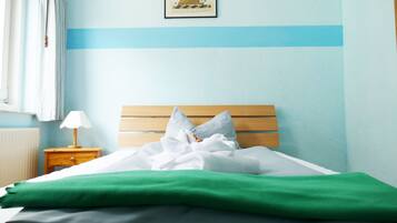 A neatly made bed with white and green linens, a wooden headboard, and a small bedside table with a lamp.