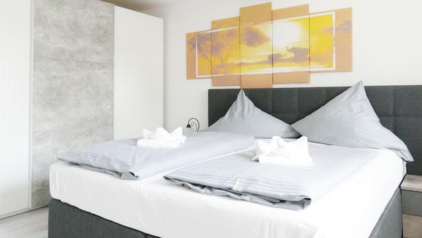 A modern hotel room with a large bed, grey bedding, and a wall-mounted artwork depicting a sunset. - Hotel Weserstuben (Bodenwerder)