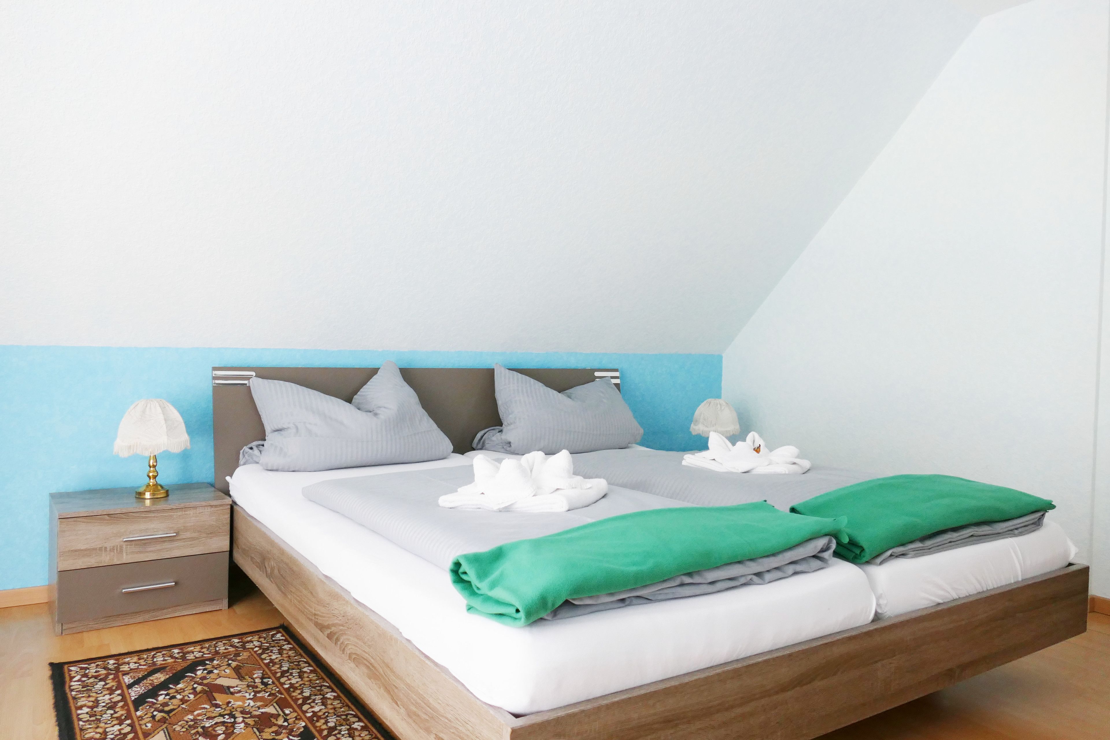 A neatly made bed with white and green linens, a bedside table with a lamp, and a patterned rug.