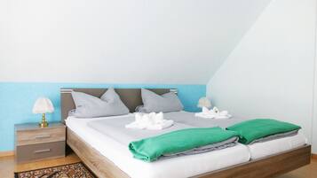 A neatly made bed with white and green linens, a bedside table with a lamp, and a patterned rug.