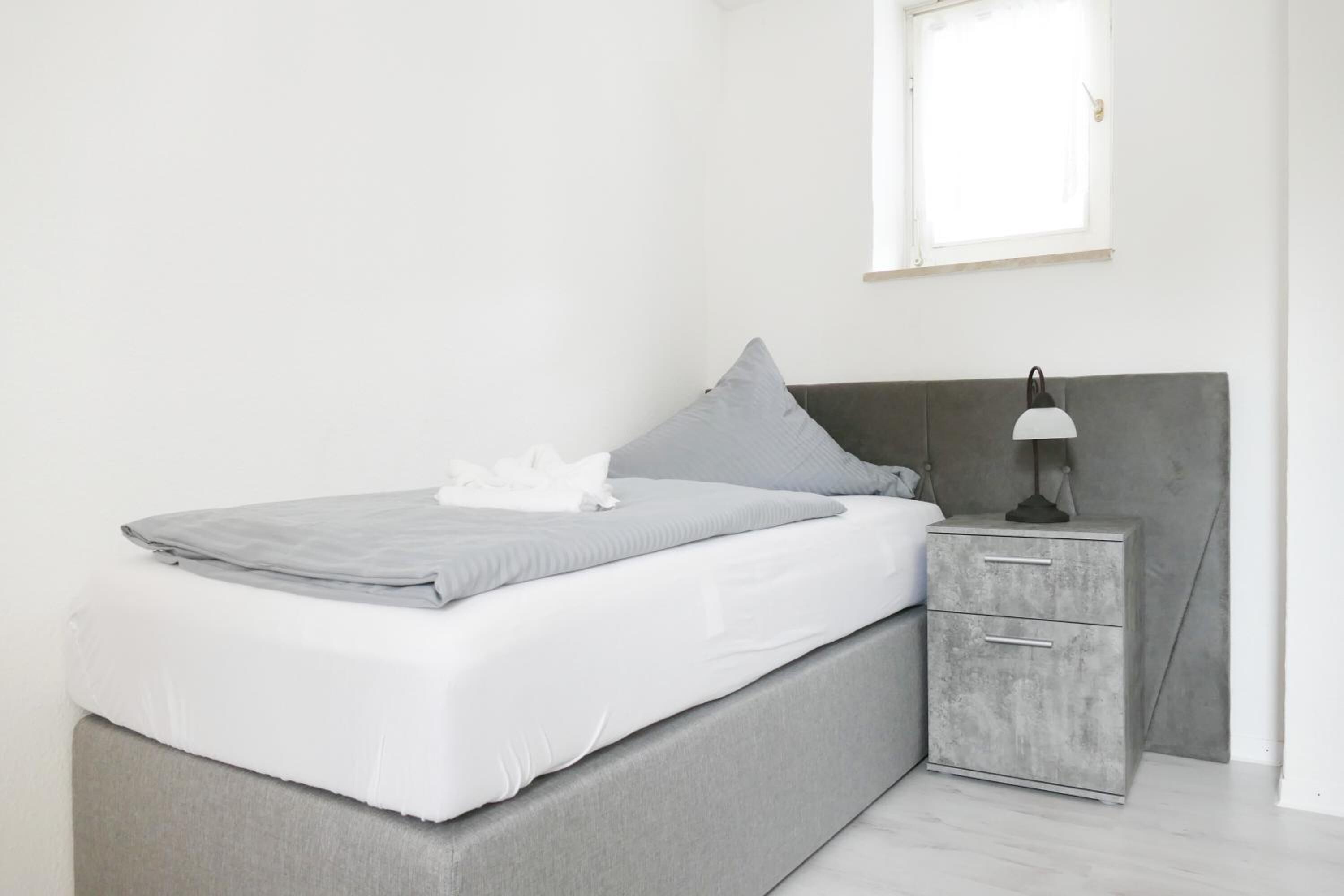 Un dormitorio minimalista con cama, mesita de noche y ventana.