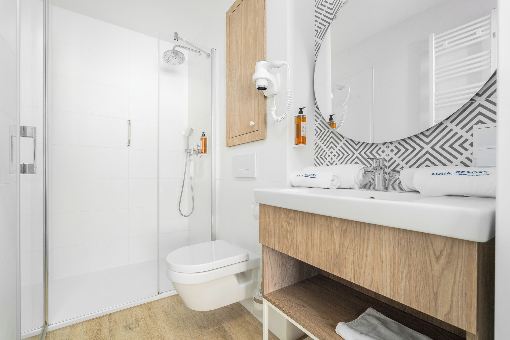 Un baño moderno con ducha de vidrio, inodoro blanco y tocador con espejo y perchero.