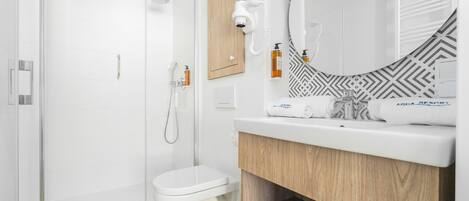 Un baño moderno con ducha de vidrio, inodoro blanco y tocador con espejo y perchero.
