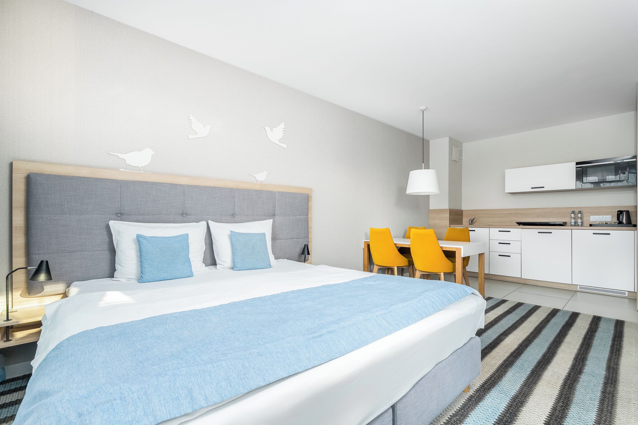 Moderni hotellihuone, jossa on suuri sänky, työpöytä ja pieni keittiönurkkaus.