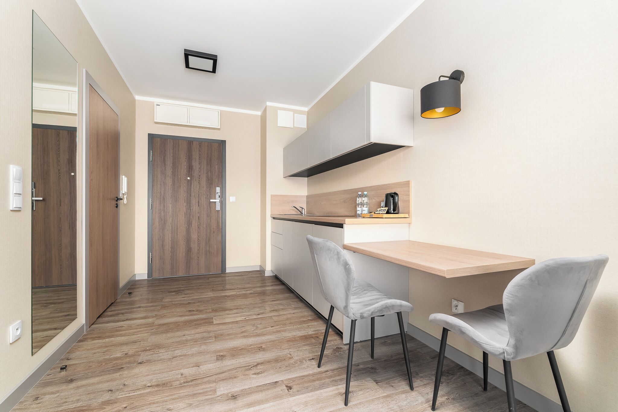 A modern kitchen with a wooden countertop, two grey chairs, a built-in stove, and a wall-mounted light fixture.