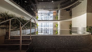 Un espace piscine intérieur moderne, doté d’une paroi en verre, d’un escalier en métal et de plantes en pot.