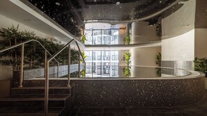 Un espace piscine intérieur moderne, doté d ’une paroi en verre, d’un escalier en métal et de plantes en pot.