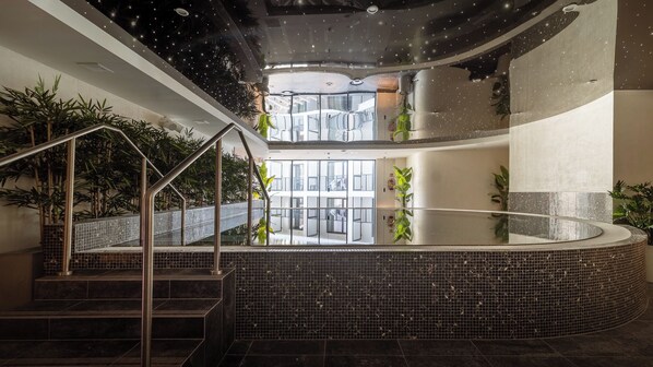 Un área de piscina interior moderna con barandilla de vidrio, escaleras de metal y plantas en macetas.