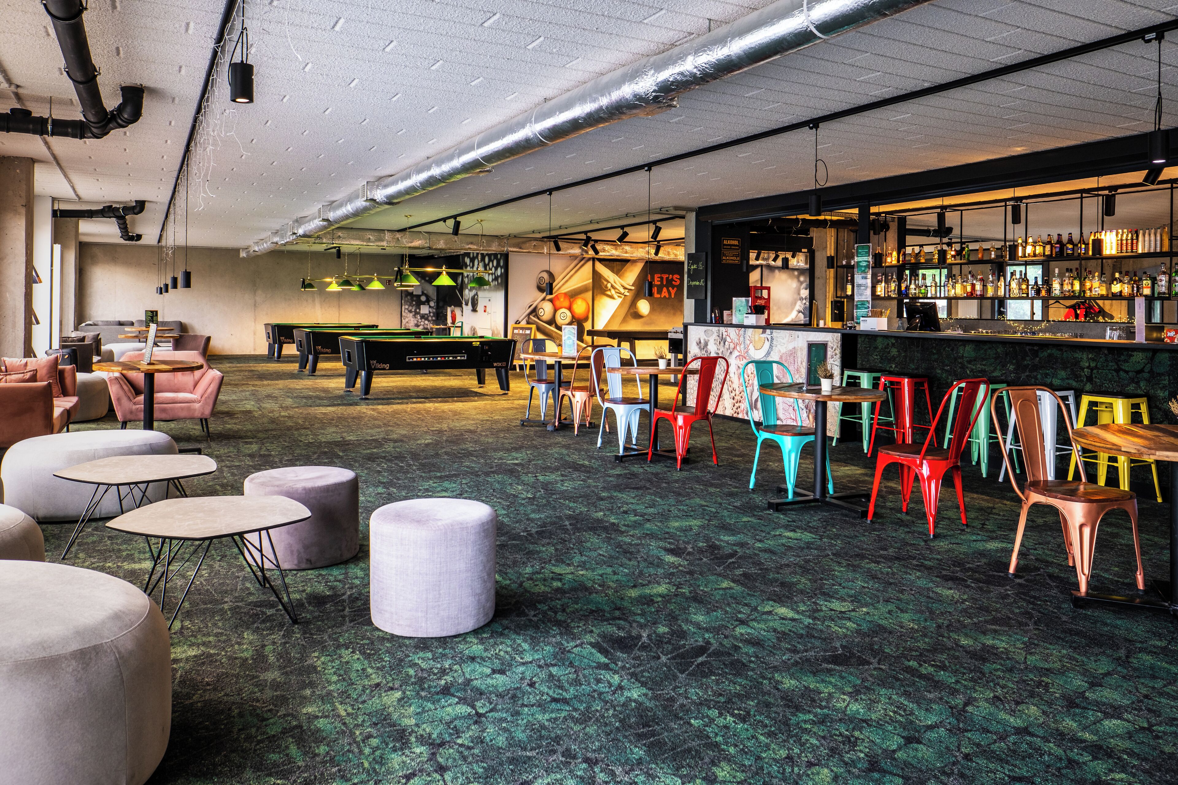 A bar area with pool tables, colorful chairs, and a bar stocked with bottles.