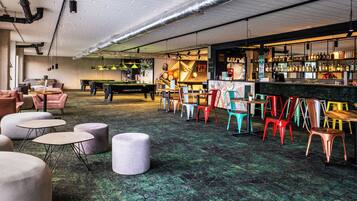 A bar area with pool tables, colorful chairs, and a bar stocked with bottles.