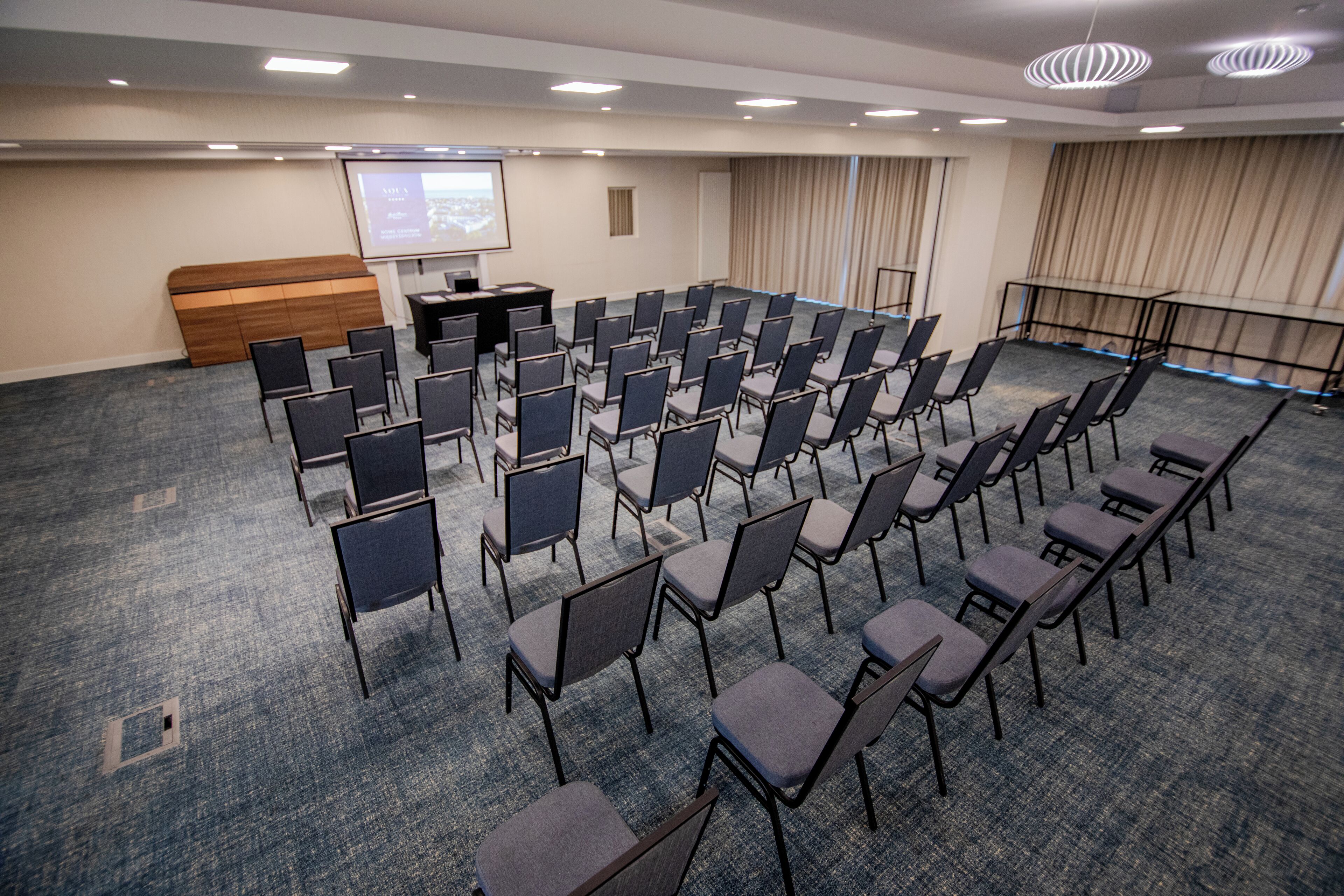 Un salón de conferencias con filas de sillas, un atril y una pantalla de proyección.