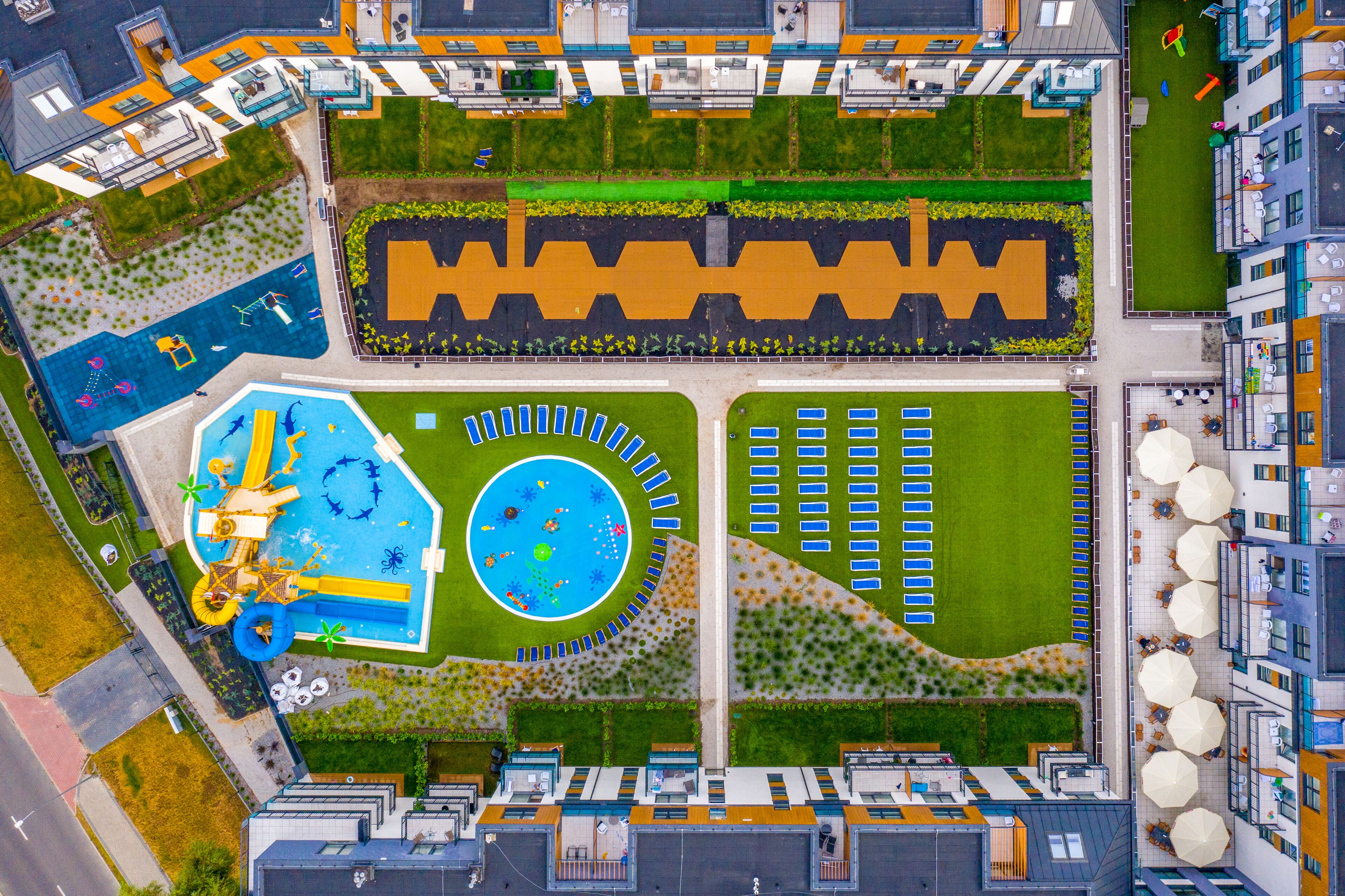 An aerial view of a hotel with a swimming pool, a children's play area, and a parking lot.