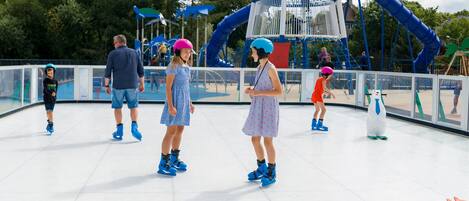 A group of children roller skating on a smooth, white surface with a large blue slide structure in the background.