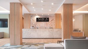 Un espace d’accueil avec un comptoir de réception en bois, une grande enseigne indiquant « AQUA RESORT » et un tapis à motifs.